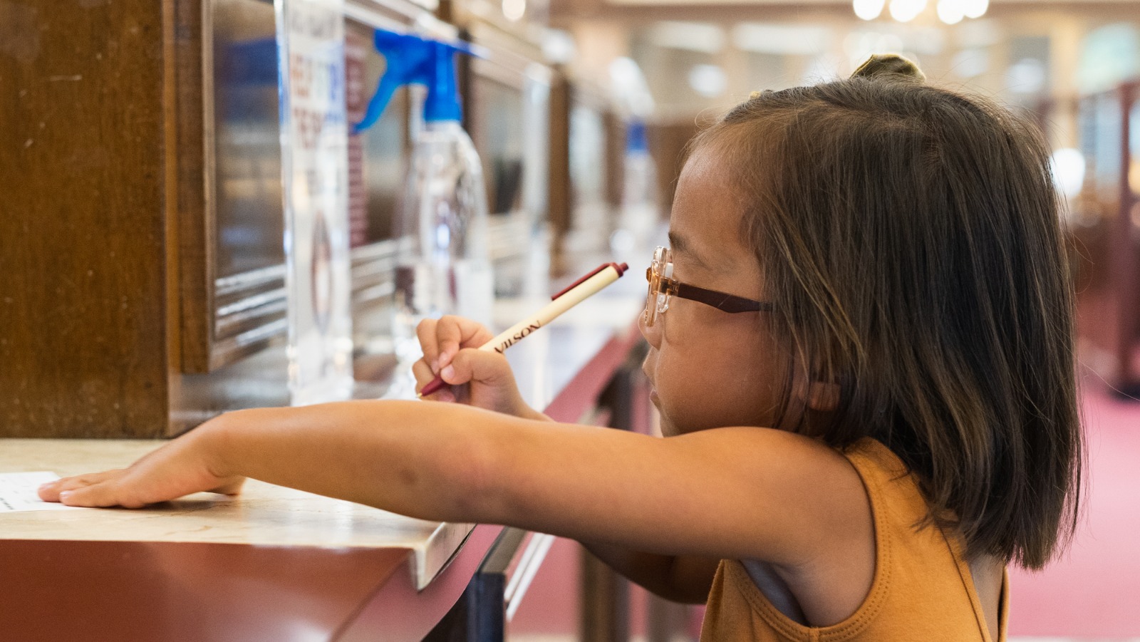 Child at teller window filling out deposit slip.