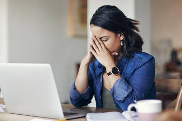 A woman sitting in front of a laptop with her face in her hands.