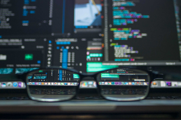 A pair of glasses in front of a laptop with a lot of data on the screen.