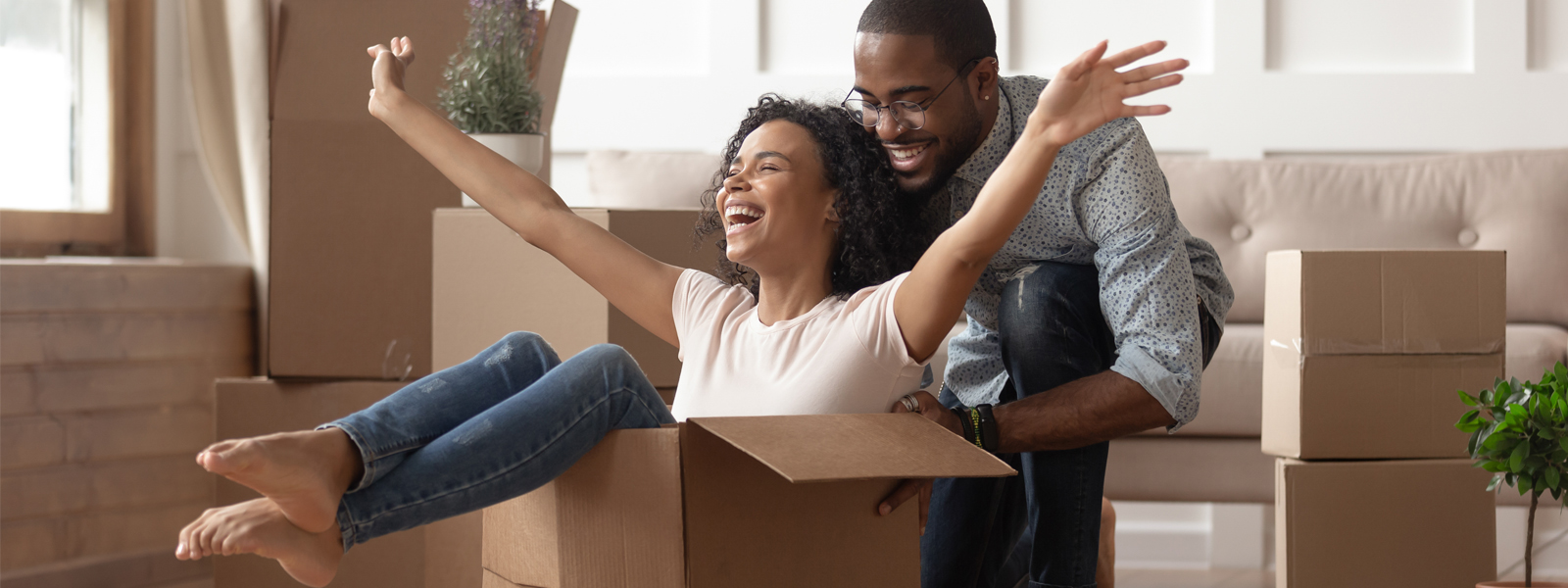 A woman sitting in a moving box and her husband behind her.
