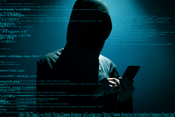 A person with a hood on looking at a phone with code written over the image.