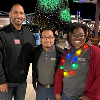 A group picture of three people outside around the holidays.